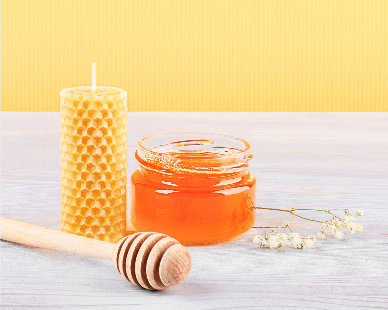 Beeswax candle, glass jar with honey, honey dipper and flower.